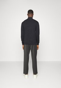 Pull en maille gris foncé avec un col montant, associé à un pantalon gris sur mesure et des baskets blanches, vu de dos.