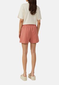 Lichte, koraalroze shorts met een elastische tailleband en zakken aan de zijkant. Draag een loszittend, crèmekleurig t-shirt bij.