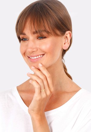 Gold ring with infinity design on a slender finger, worn with a white top. Smooth texture and delicate outline are notable features.