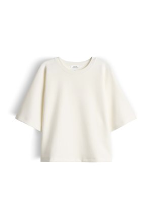 Crèmekleurig oversized T-shirt met korte mouwen en een ronde hals, met een klein label aan de binnenkant van de hals, tegen een witte achtergrond.