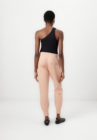 Light pink sweatpants with elastic waistband and single back pocket, paired with a black one-shoulder top. Black flat shoes complete the look.