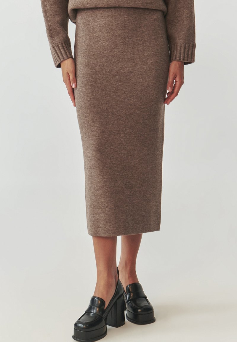 Jupe midi en tricot marron avec une silhouette ajustée. Texture douce, taille côtelée. Assortie avec des chaussures à plateforme noires épaisses.