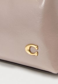 Ροζ δερμάτινη τσάντα με λεία υφή και στρογγυλεμένο σχήμα. Διαθέτει ένα εντυπωσιακό χρυσό λογότυπο μεταλλικής επένδυσης στο πλάι.