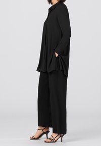 Musta, rento pusero, jossa on kaulus ja sivutaskut, yhdistettynä leveälahkeisiin mustiin housuihin ja mustiin nauhaliivikenkihin. Sileä kangas.