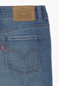 Vaqueros de denim de Levi's en color azul claro, con un parche de cuero marrón en la cintura y un diseño distintivo en el bolsillo trasero.