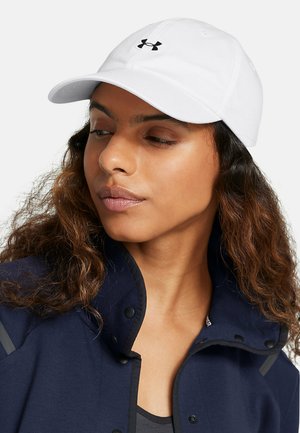 Witte stoffen pet met een gebogen klep, met een zwart logo aan de voorkant. De drager heeft golvend bruin haar en draagt een donkere jas.