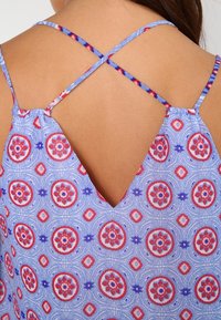 Modrý vzorovaný top s nastavitelnými zkříženými ramínky. Obsahuje květinové motivy v červené a fialové barvě. Lehká tkanina s vykrojeným zadním dílem ve tvaru V.