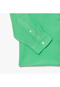Maglietta verde a maniche lunghe realizzata in tessuto leggero, con polsini ripiegati e superficie testurizzata. Il design è semplice e moderno.