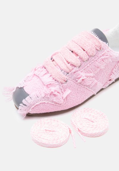 Baskets roses texturées avec des bords effilochés, un bout gris, et deux paires supplémentaires de lacets roses assortis sur un fond blanc.