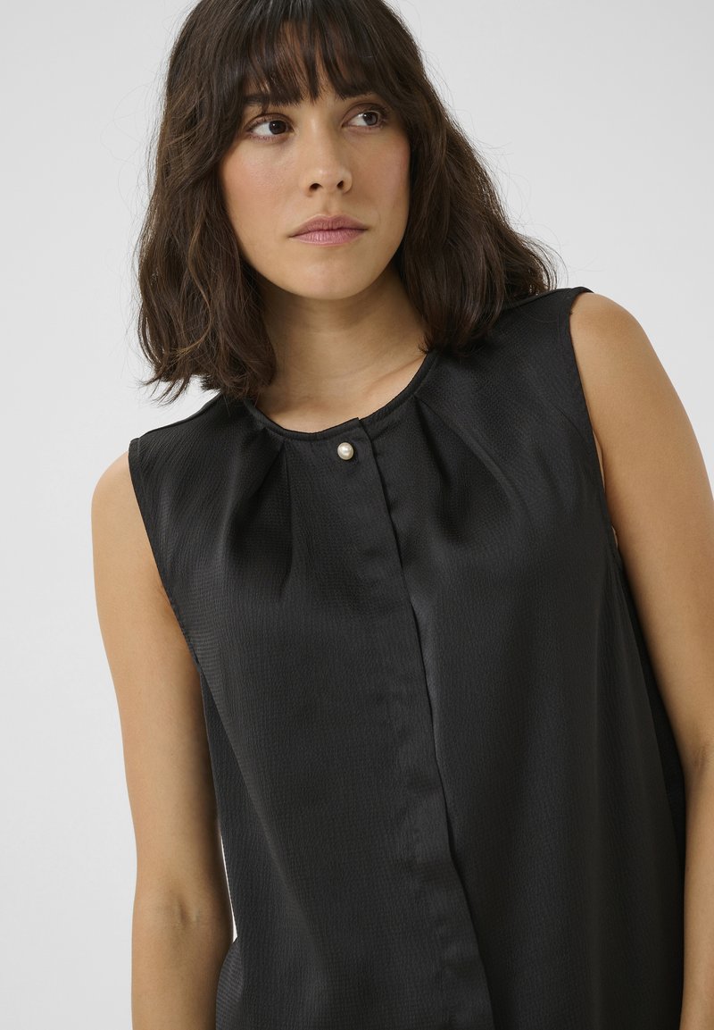 Czarna bezrękawnikowa bluzka z teksturowanej tkaniny. Posiada okrągły dekolt, fałdy oraz dekoracyjne zapięcie na perłowy guzik z przodu.
