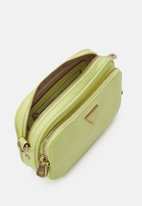 Borsa a tracolla verde lime con doppia cerniera, hardware color oro e un accento con logo triangolare; texture liscia con un design sottile.
