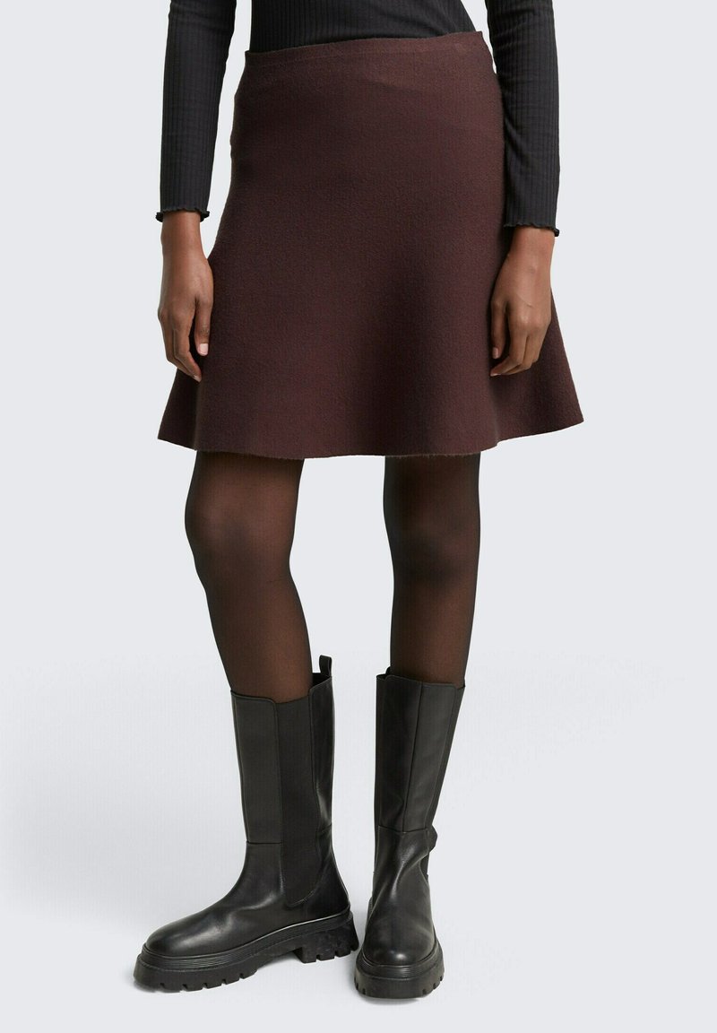 Bordeaux flared rok gemaakt van gestructureerde stof, gecombineerd met zwarte leren kniehoge laarzen met een dikke zool en een elastische zijpaneel.