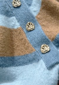 Cardigan en laine douce, présentant un motif de blocs marron et bleu. Boutons décoratifs argentés avec un design tressé.