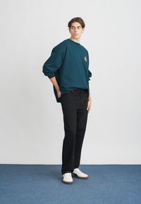 Sweatshirt in teal with a round neckline and oversized sleeves, paired with black straight-leg jeans and white sneakers.