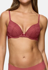 Malinový krajkový podprsenka s hlubokým výstřihem, polstrovanými košíčky a nastavitelnými ramínky. Obsahuje malou dekorativní mašličku uprostřed.