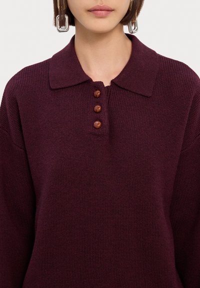 Jersey burdeos con cuello tipo polo, con tres botones marrones en la tapeta y una tela texturizada. Corte relajado.