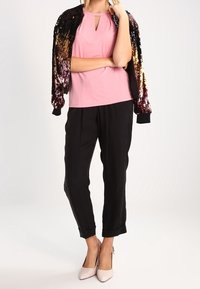 Top rosa senza maniche con scollatura a chiave, giacca bomber nera con paillettes, pantaloni neri a sigaretta e tacchi a punta beige chiaro.