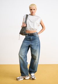 White cropped top with elastic hem, blue wide-leg jeans, gray patterned handbag, and chunky white and brown sneakers.