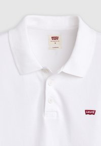 Hvitt bomullspolo med klassisk krage, tre-knappers placket, og en liten rød Levi's-logo på venstre bryst.
