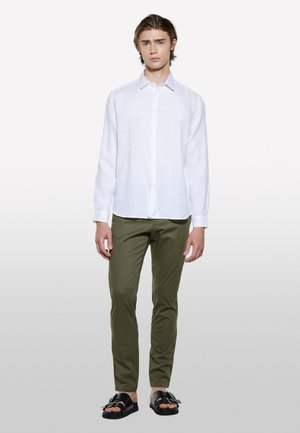 Camicia bianca in lino a maniche lunghe, con bottoni sul davanti, abbinata a chinos verde oliva e sandali neri con dettaglio a fiocco.