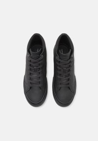 Para czarnych sneakersów na sznurówki o niskiej wysokości kostki, z widocznymi przeszyciami i z logotypem na języku, widziana z góry na białym tle.