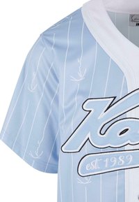 Világoskék sportmez függőleges fehér csíkokkal, kerek fehér gallérral, és merész fekete-fehér logóval, amely az "est. 1989." feliratot tartalmazza. Struktúrált anyag.
