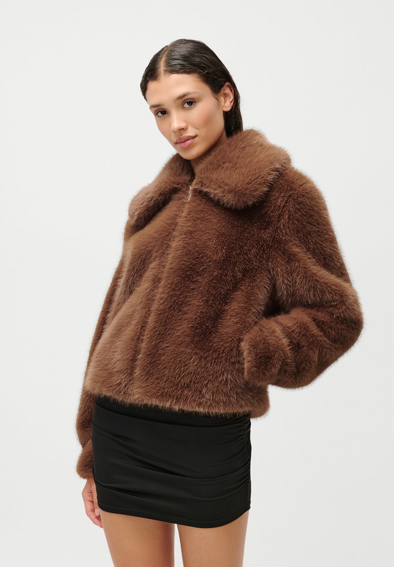 Καφέ ψεύτικο γούνινο μπουφάν με φαρδύ γιακά, κλείσιμο με φερμουάρ και μακριά μανίκια. Μαλακή υφή, κοντό σχέδιο, συνδυασμένο με μια μαύρη μίνι φούστα.