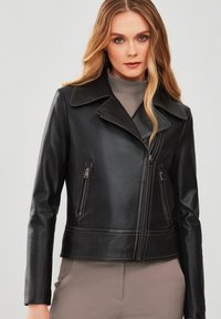 Zwarte leren jas met een brede kraag, ritssluiting aan de voorkant, zijzakken en contrasterende stiksels. Gladde textuur met een aansluitend design.
