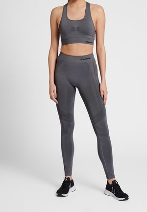 Top corto atletico grigio e leggings con pannelli testurizzati, design aderente e logo del marchio. Scarpe da corsa nere completano l'outfit.