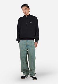 Black ribbed sweater with a half-zip collar and embroidered logo, paired with light blue wide-leg jeans and black and white sneakers.