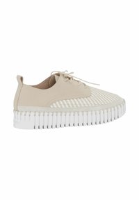 Zapatilla beige con parte superior tejida texturizada, puntera redonda y suela gruesa blanca estriada. Presenta un diseño con cordones y una pequeña lengüeta en el talón.