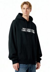 Sweat à capuche noir avec une poche avant, portant un texte blanc qui dit : "JE DOIS RÉUSSIR PARCE QUE J'AIME LES CHOSES CHÈRES."