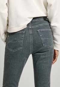 Tmavě šedé džíny slim fit, se dvěma zadními kapsami a subtilními detaily prošívání. Pas má na zadní straně černou etiketu.