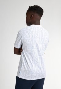 Camiseta blanca con un diseño estampado que presenta letras grandes de color azul claro. Manga corta y escote redondo, confeccionada con una tela suave.