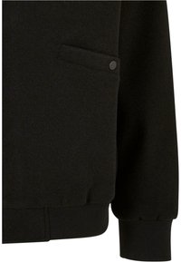 Sudadera negra con un acabado texturizado, que presenta un bolsillo con botones y puños de canalé. La tela parece suave y cálida.