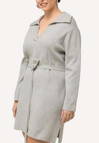 Abito in poliestere grigio con scollatura a V, maniche lunghe e cintura da annodare in vita; presenta una vestibilità comoda e spacchi laterali per facilitare il movimento.