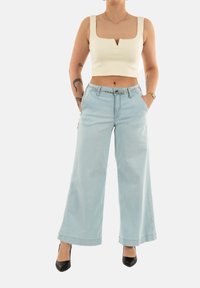 Jeans de pierna ancha en azul claro con una cintura alta, que cuentan con un cinturón con detalles en plata, y un top corto ajustado en crema con escote cuadrado y tirantes cortos.