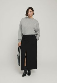 Felpa grigia con maniche lunghe, abbinata a una gonna maxi nera con uno spacco frontale. Stivali neri in pelle alla caviglia e una borsa nera con borchie.