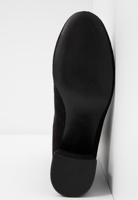 Semelle de chaussure en daim noir avec une finition lisse et des rainures texturées ; taille indiquée 36. La semelle a une forme arrondie et une légère courbe au talon.