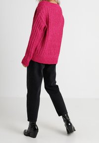 Pull oversize en tricot texturé rose vif, associé à un pantalon noir taille haute et des bottines noires brillantes.