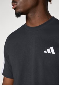 Zwarte katoenen t-shirt met een ronde hals, met een witte gestreepte logo op de borst en witte accenten op de mouwen.