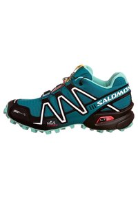 Turkos sportig sko med svarta detaljer, med ett texturerat ovandel, aggressivt mönster under sulan och ett snabbt snörningssystem. Märkbar logotyp på sidan.