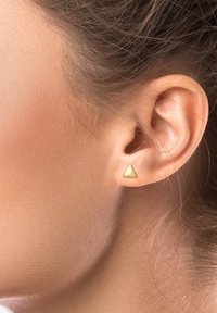 Cercei cu stud în formă de triunghi auriu, design mic și minimalist, cu o textură mată netedă, așezat într-o ureche perforată.