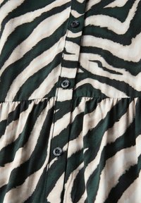 Tessuto a stampa zebra verde e crema con chiusura a bottoni; bottoni neri; dettaglio arricciato in vita; texture liscia.