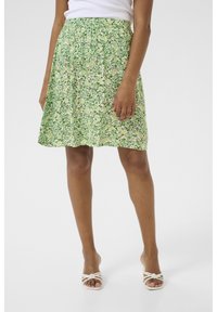 Grøn blomsterkjole med en samlet talje, der har små hvide og mørkegrønne blomster på en lys gul baggrund. Midt-længde design.