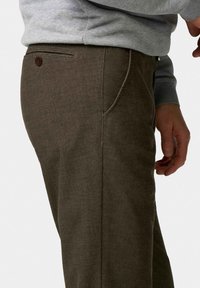 Bruine broek van een gestructureerde stof, met een achterzak met knoopsluiting en een getailleerde pasvorm. Strakke tailleband zichtbaar.