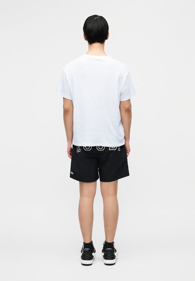 Λευκό κοντομάνικο μπλουζάκι συνδυασμένο με μαύρο σορτς ως το μέσο του μηρού με λευκά γράμματα σε μπλοκ. Μαύρα αθλητικά παπούτσια ολοκληρώνουν το ντύσιμο.