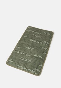 Olivovo zelený koberec s opakujúcim sa textom "CALVIN KLEIN JEANS" v rôznych odtieňoch, so hladkým povrchom a zaoblenými hranami.
