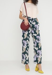 Blomstrede wide-leg bukser i mørkegrøn, med lilla og hvide blomster, parret med en beige struktureret top og gule chunky hæle.