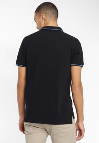 Polo noir avec des accents bleus sur le col et les manches, en coton, avec une coupe classique et des fentes sur l'ourlet.